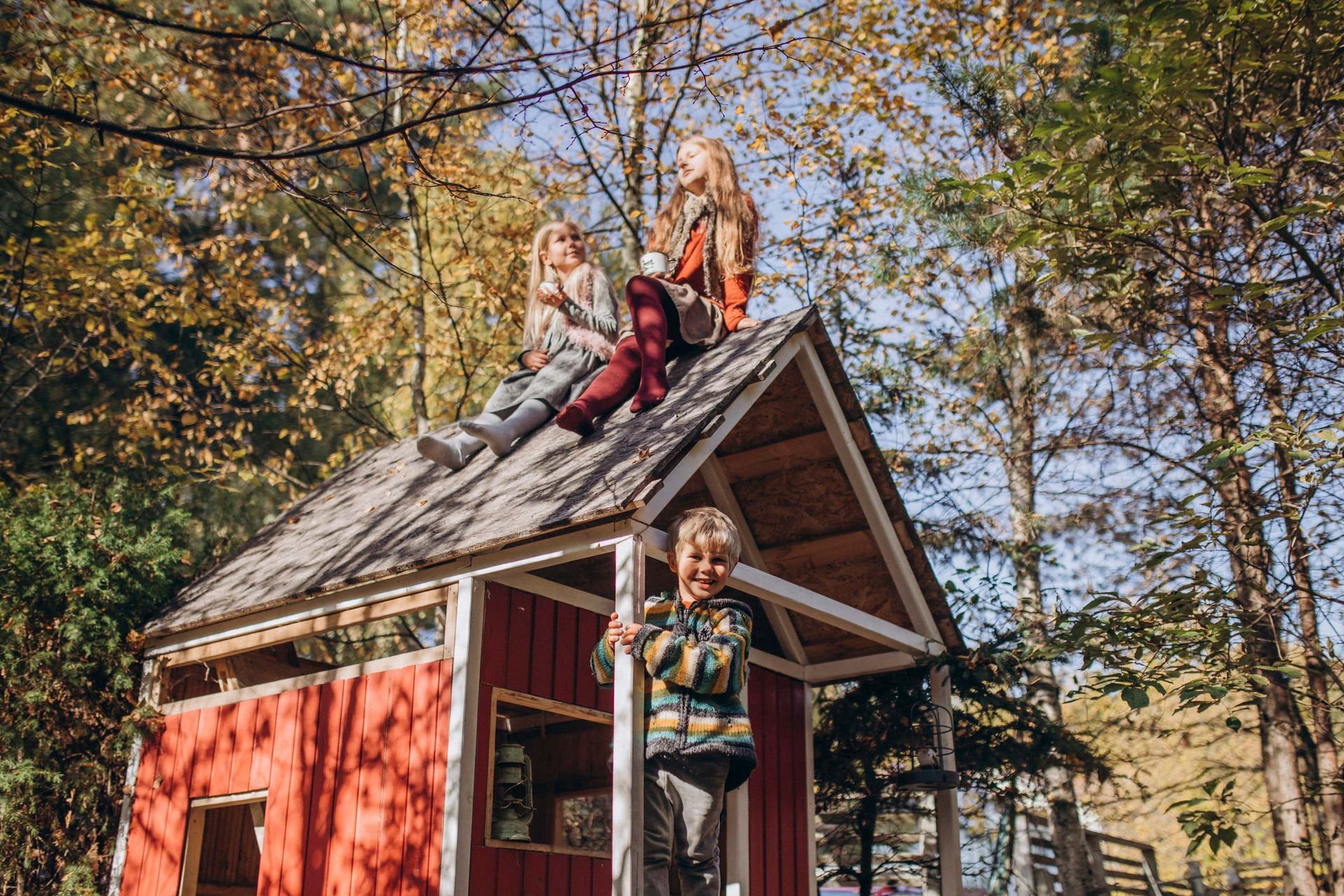 Two girls sitting on top of a shed with boy in front.