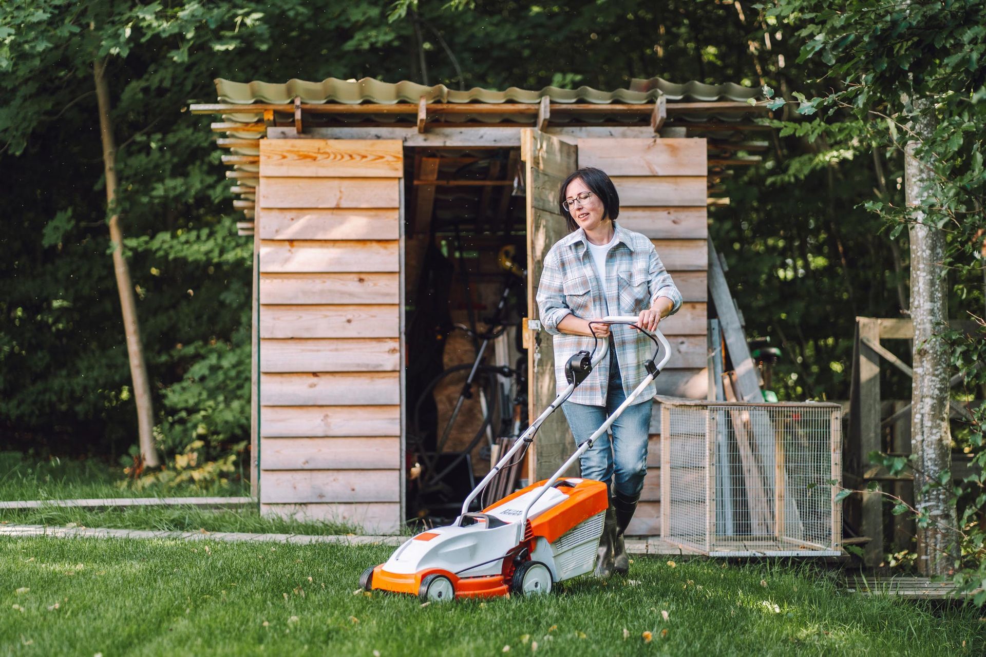 Woman bringing out lawnmower from shed in the backyard.