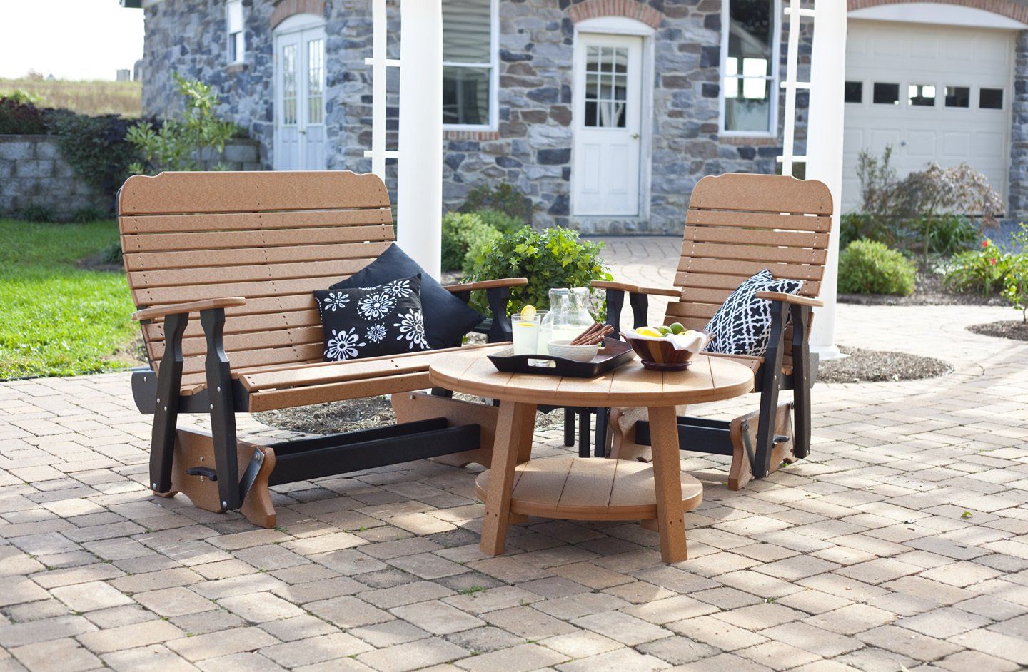 Patio set with wooden glider bench, armchairs, and round table on brick patio.