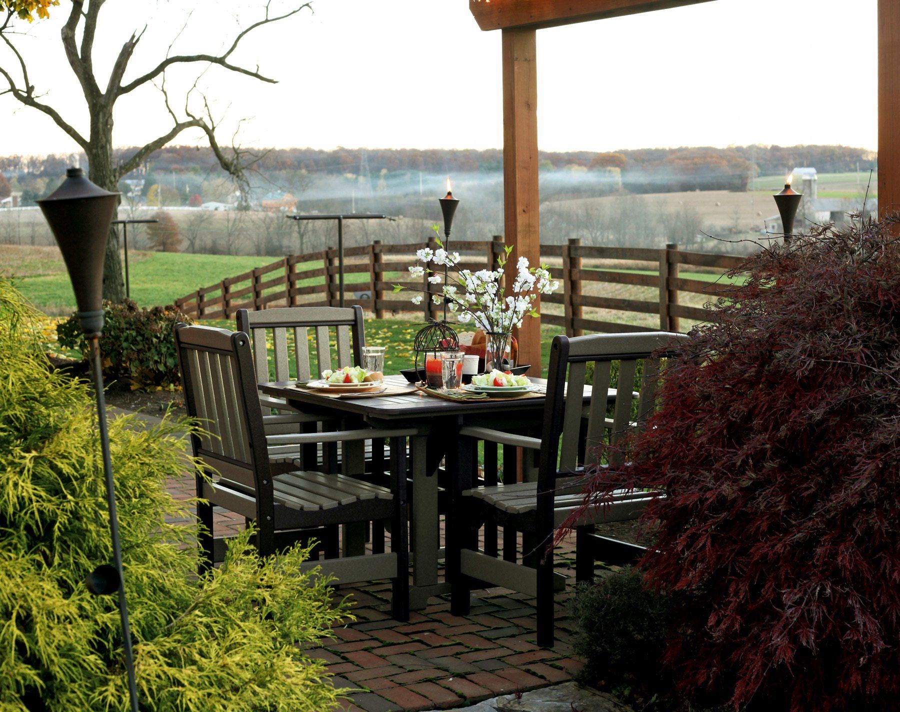 Outdoor dining set on a patio overlooking a farm with tiki torches.