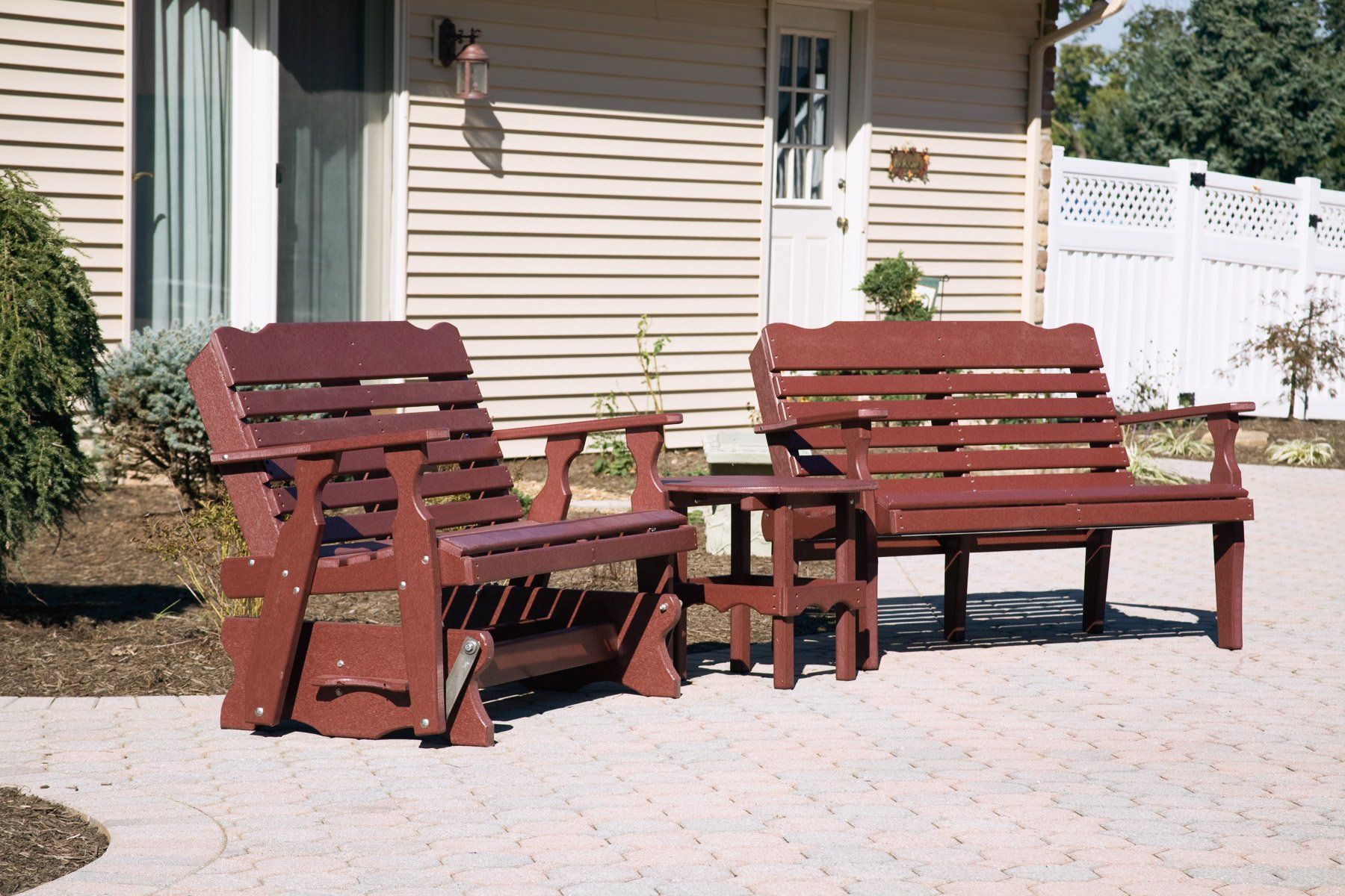 Red outdoor furniture set: glider, bench, and side table on a brick patio.