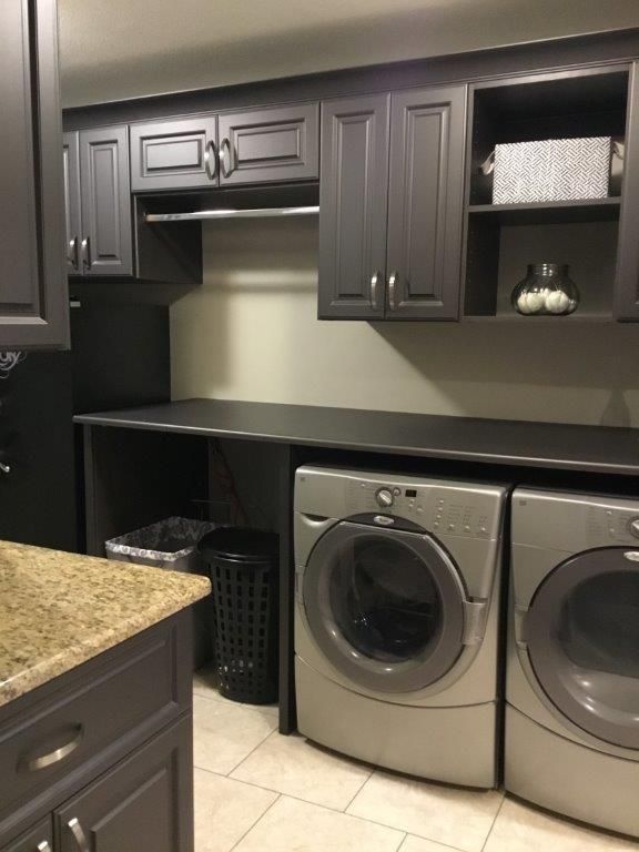 Laundry room featuring gray cabinets, a black countertop, two silver front-loading washers, and a hanging rod.
