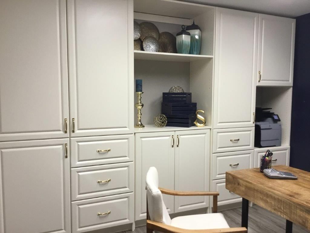 Built-in off-white cabinets with drawers and shelving surrounds a home office desk and a white office chair.