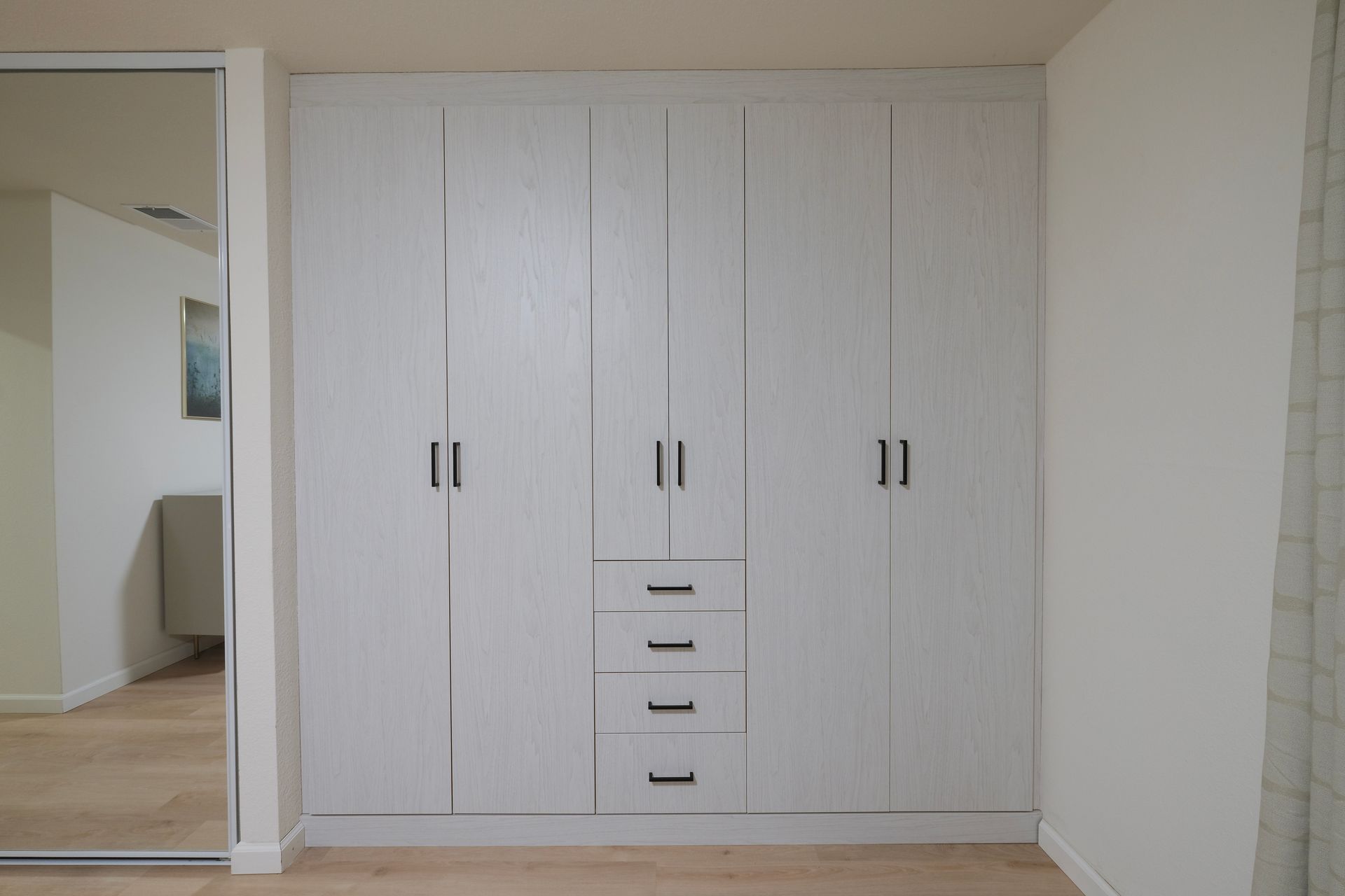 A large, white, five-door wardrobe with a column of four drawers in the center, featuring black metal handles.