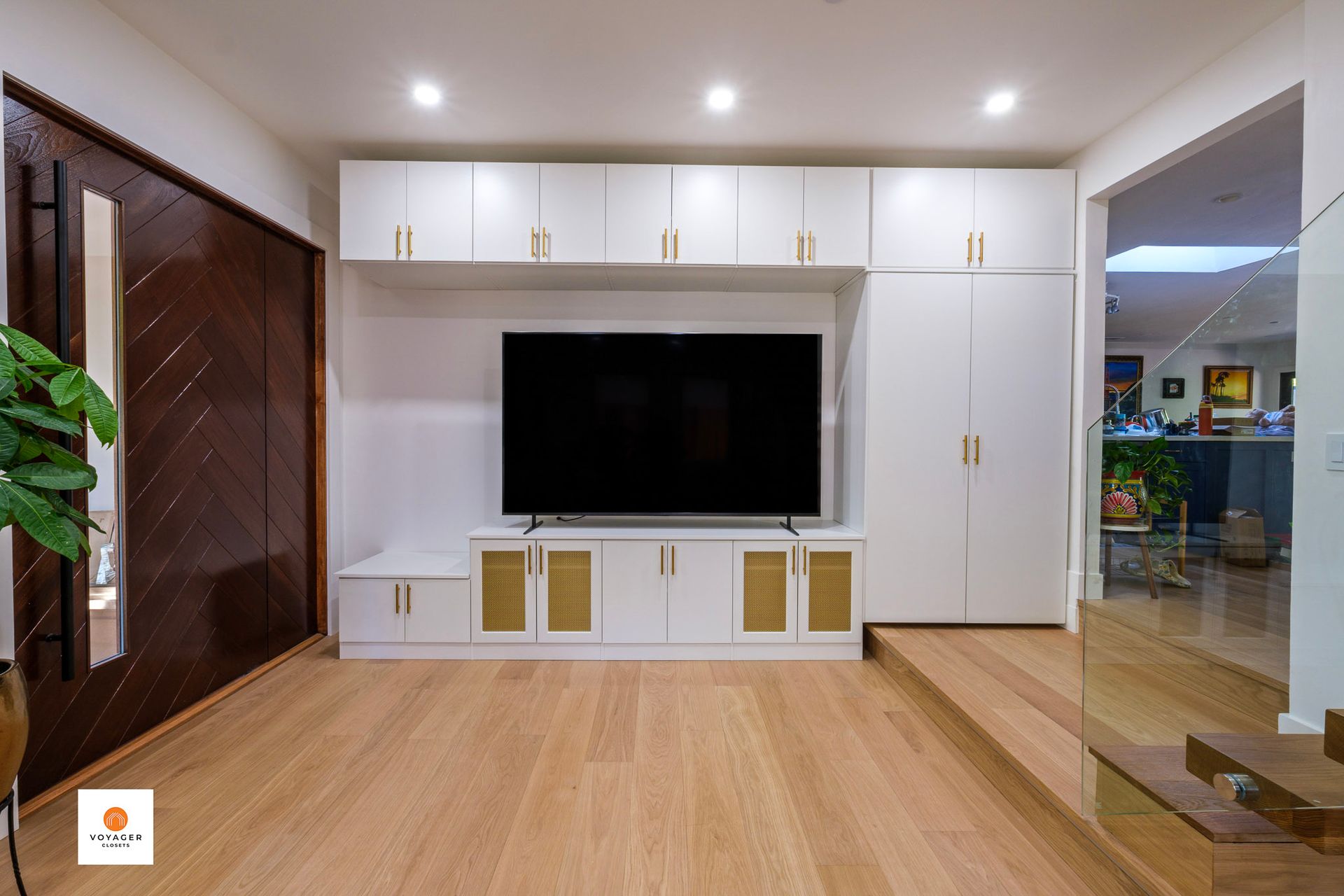 Modern living room featuring a flat-screen TV mounted on a white, custom media cabinet with light wood and wicker details.
