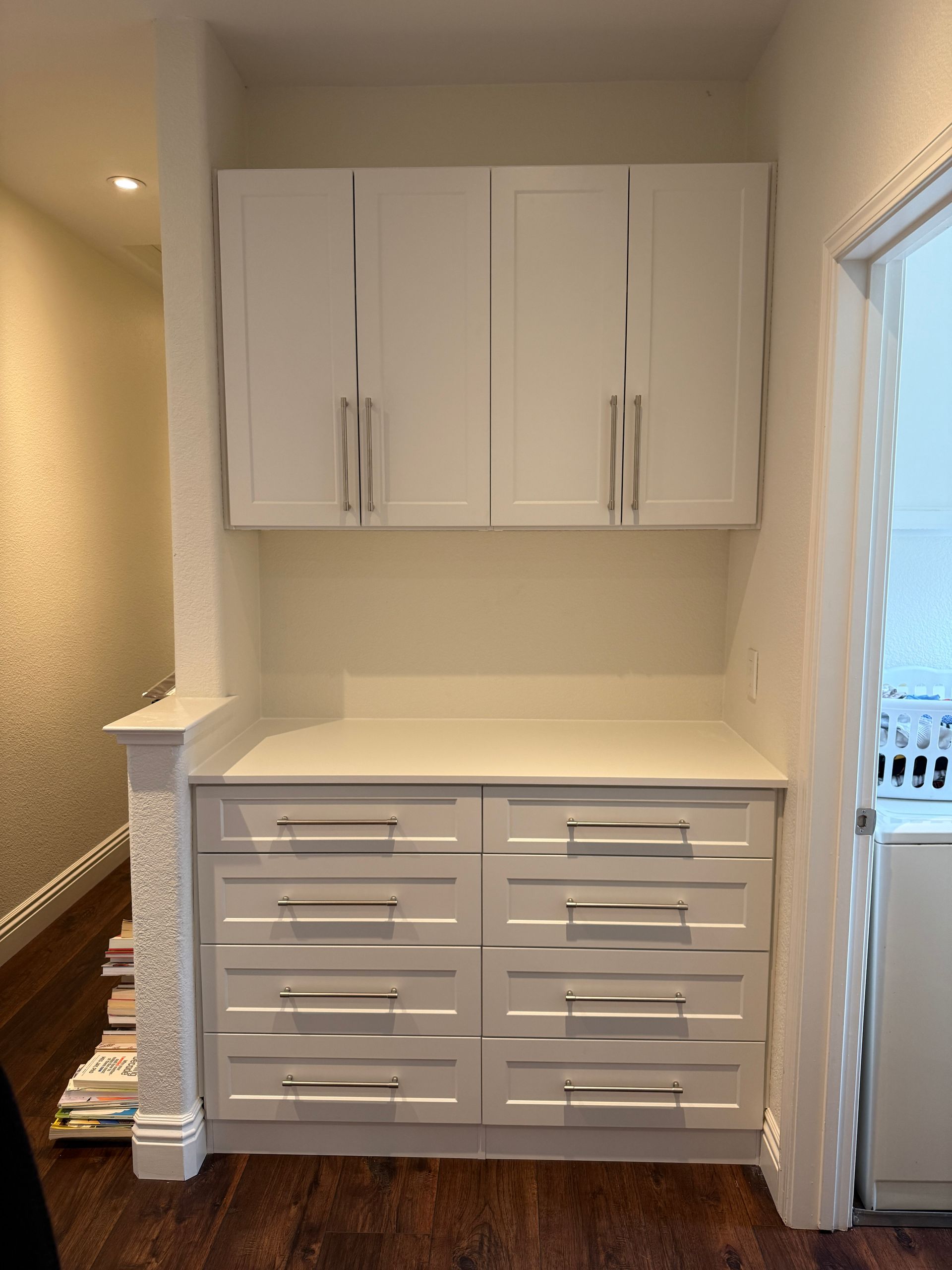 A white storage unit featuring four upper cabinet doors and eight drawers with silver handles in a hallway.