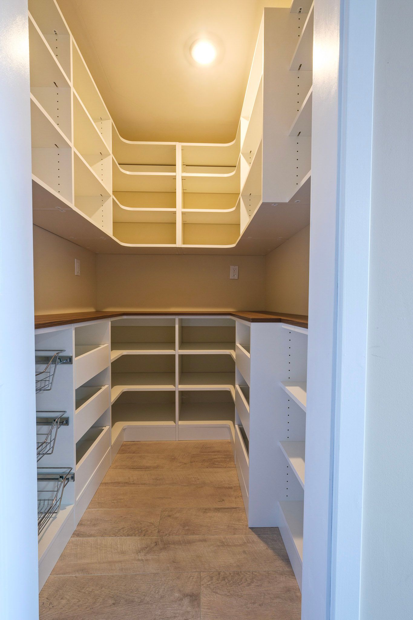 A view into a walk-in pantry with white wooden shelving and a light-colored carpet floor.
