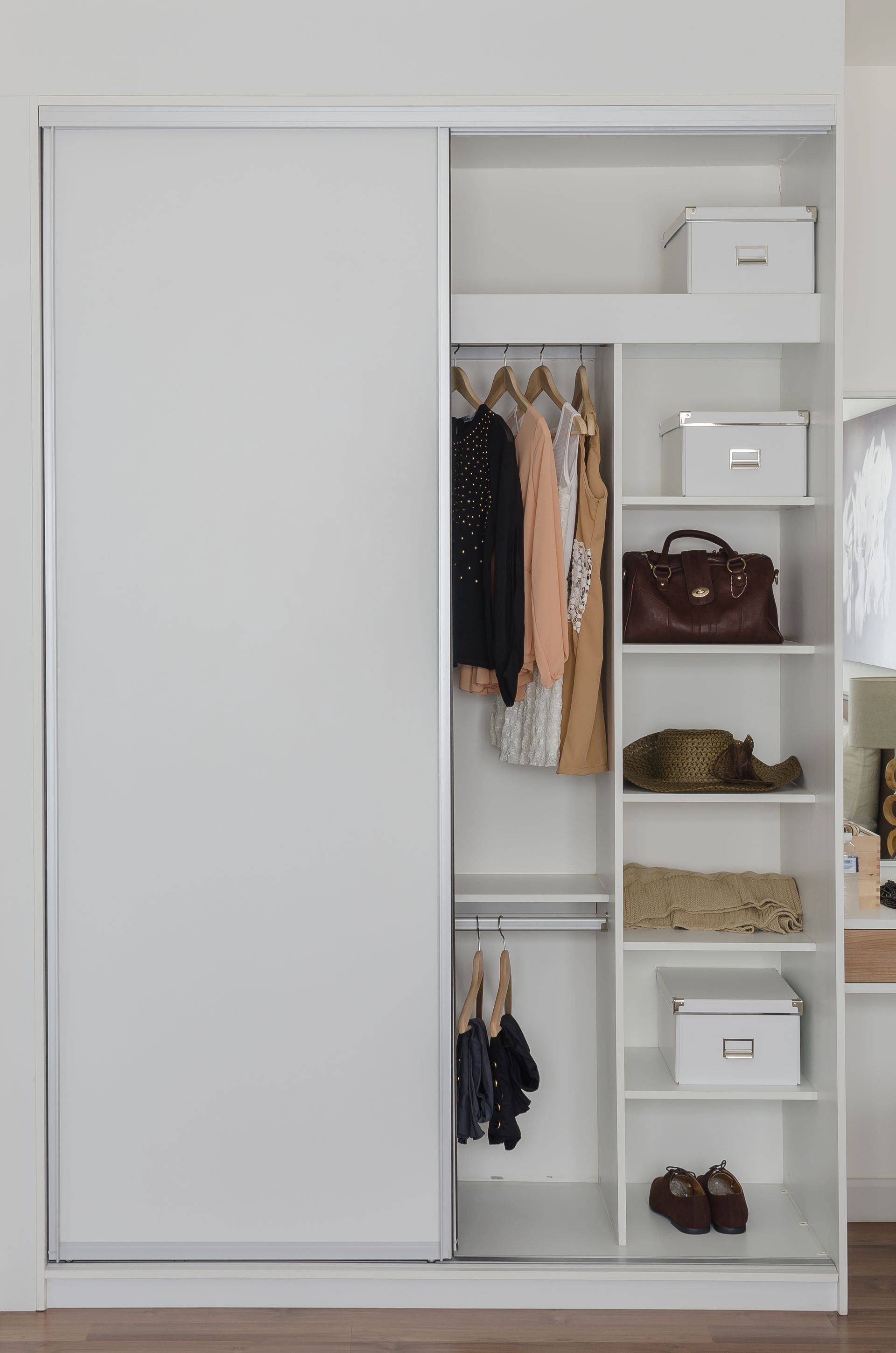 White wardrobe with sliding doors, open on the right to reveal clothing racks, shelves with boxes, and handbags.
