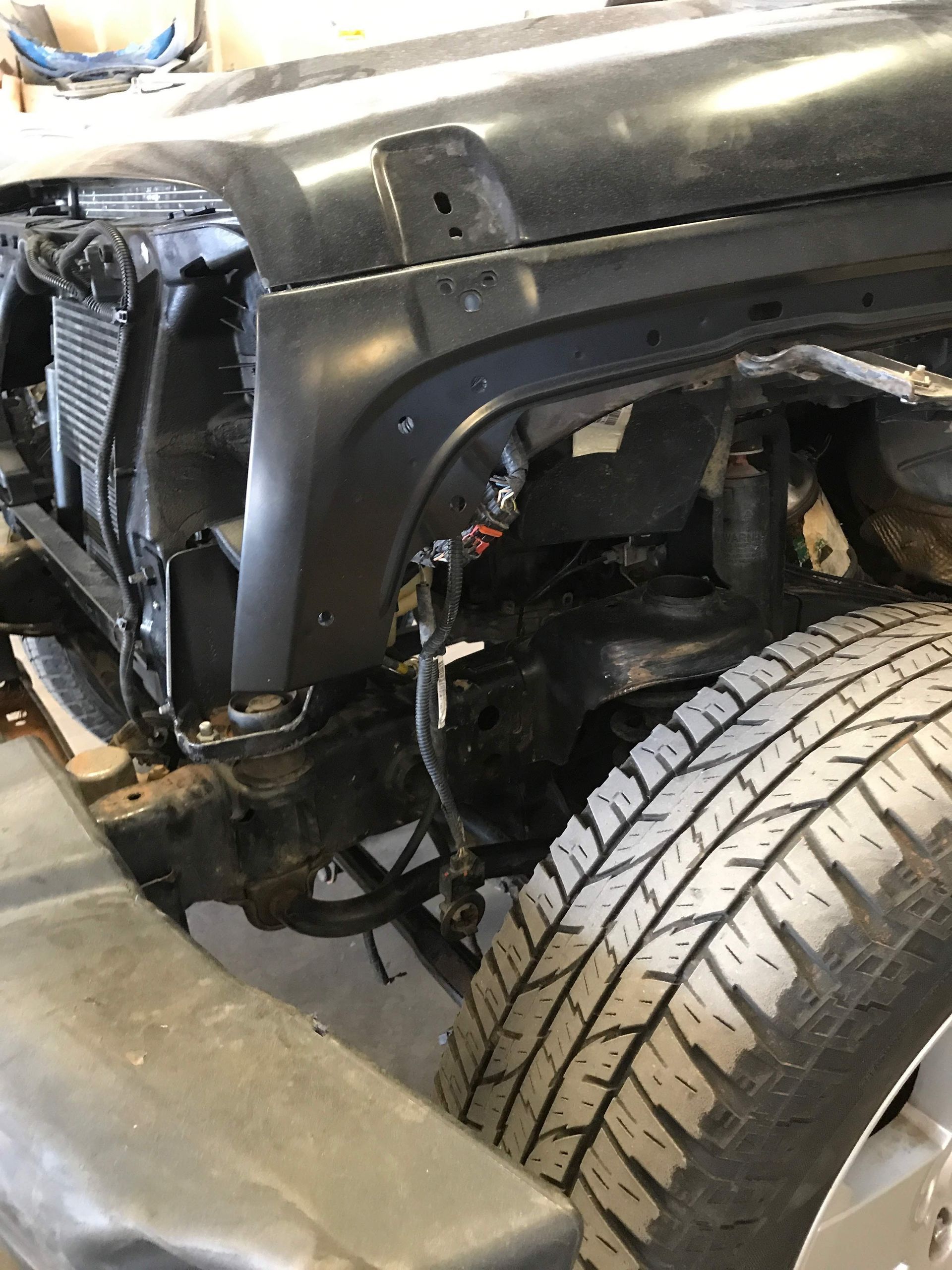 Black Jeep Wrangler front end with tire, fender, and radiator visible.