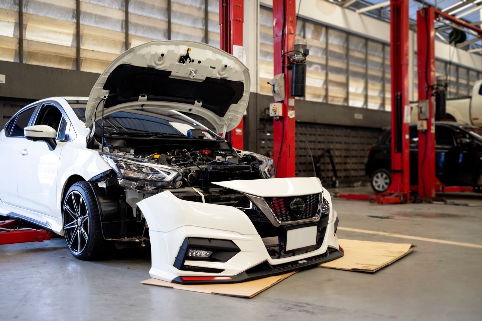 A white car with the hood open is sitting on a lift in a garage.