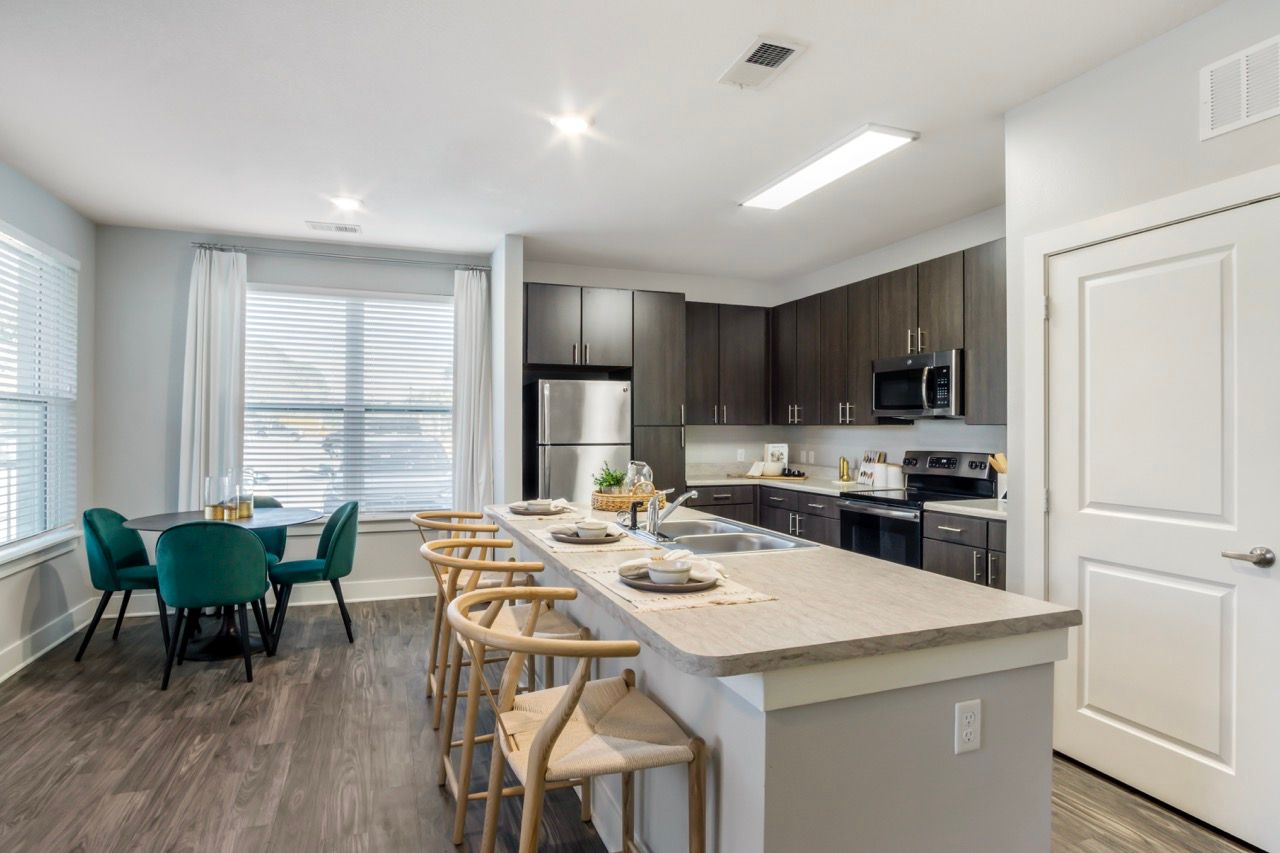 Modern apartment kitchen with large island, four bar stools, and stainless-steel appliances.