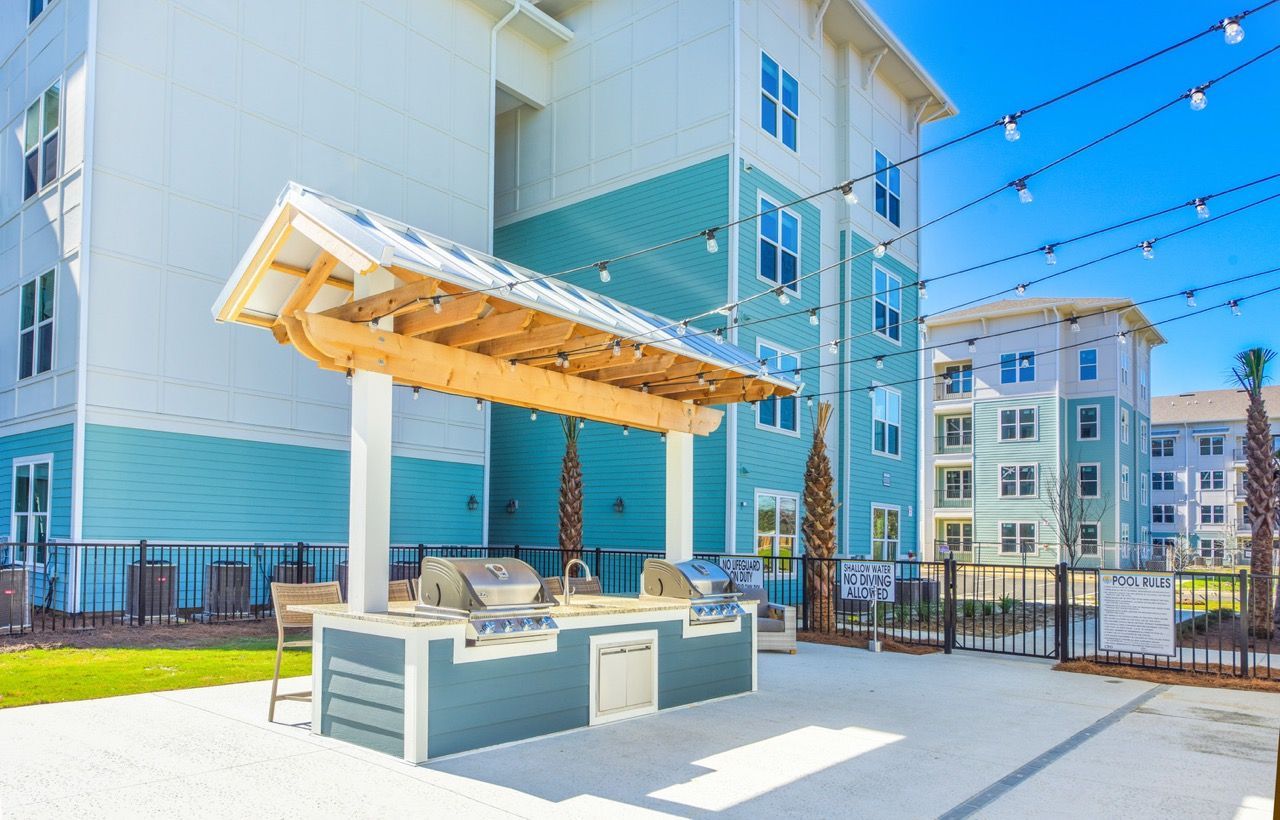 Outdoor community grilling area with two grills under a wooden pergola and string lights.