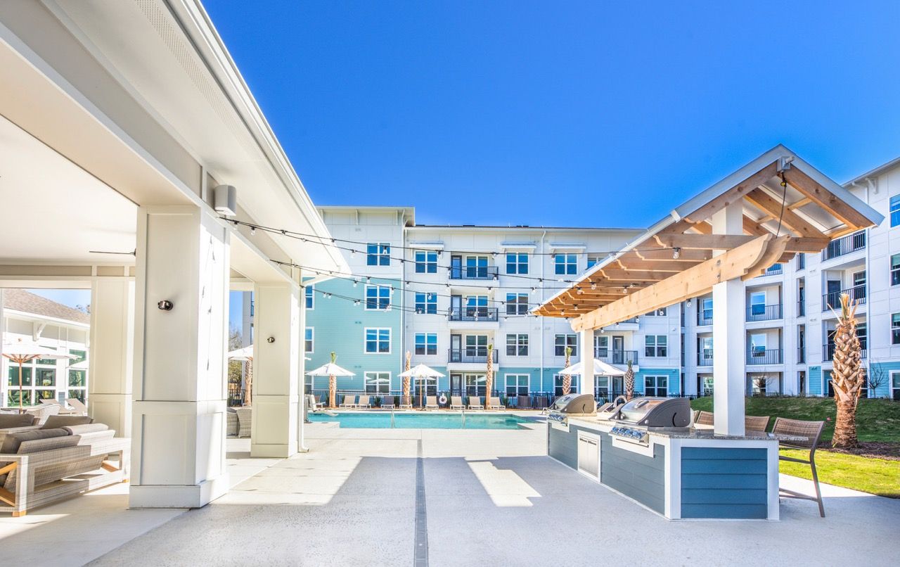 Outdoor apartment community pool area with lounge seating, umbrellas, and a grilling station.