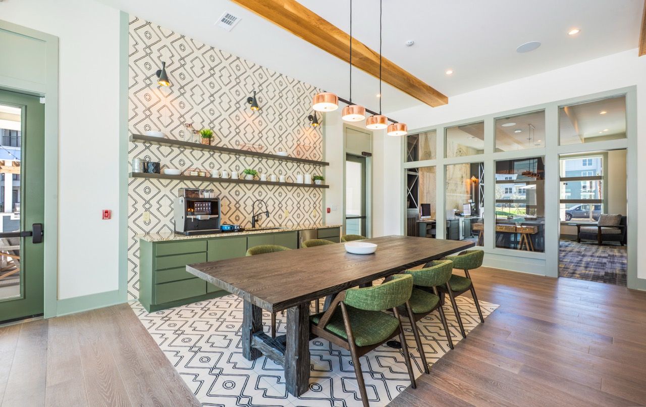 Clubhouse kitchenette with green cabinets, patterned backsplash, and a long wooden dining table.