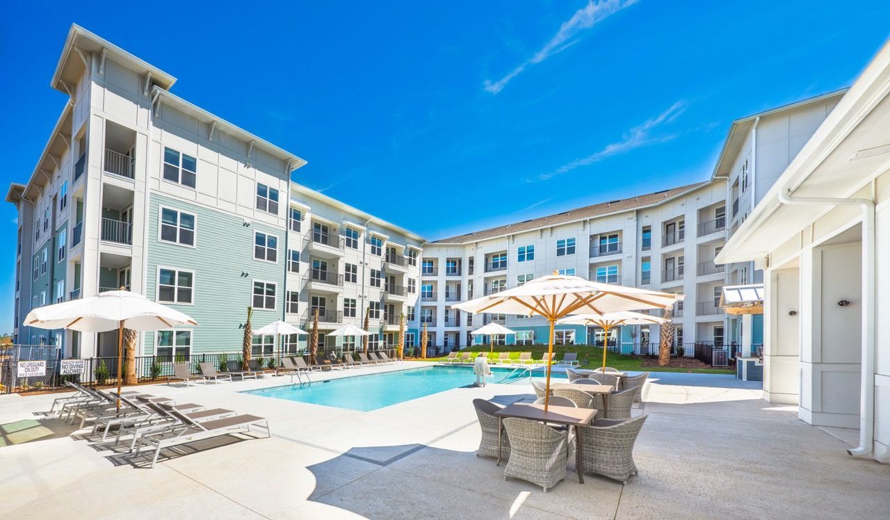 Outdoor pool area with lounge chairs and umbrellas, surrounded by a modern apartment building.