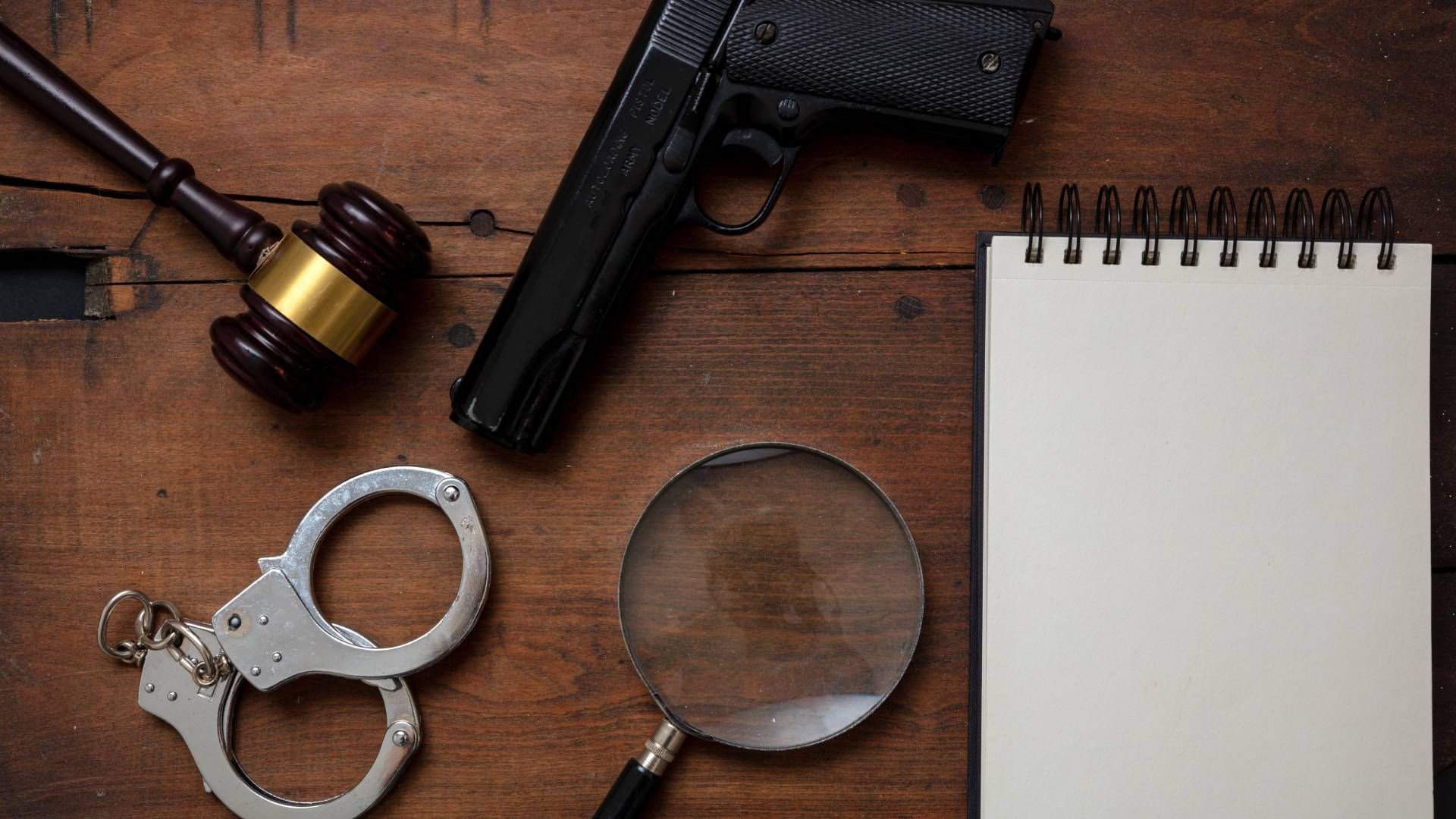 Judge’s gavel, handcuffs, gun, and a blank notepad on wooden background at JPS Law near Lexington, K