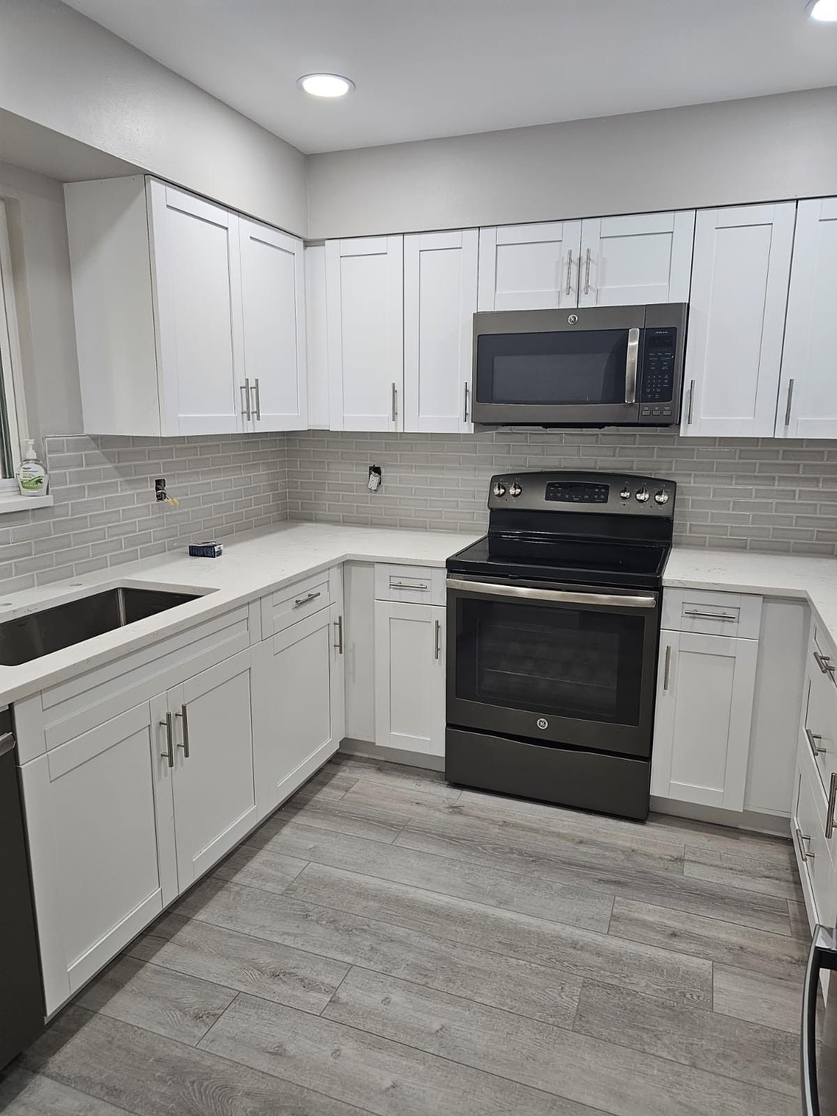 A kitchen with white cabinets , a stove , a microwave , and a sink.