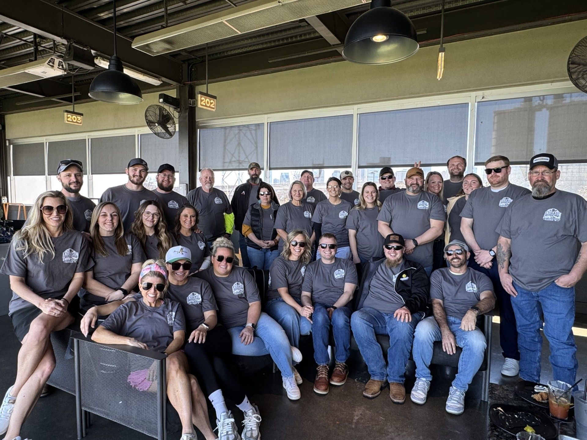 A group of people wearing matching grey shirts pose for a photo in an open-air, covered dining area.