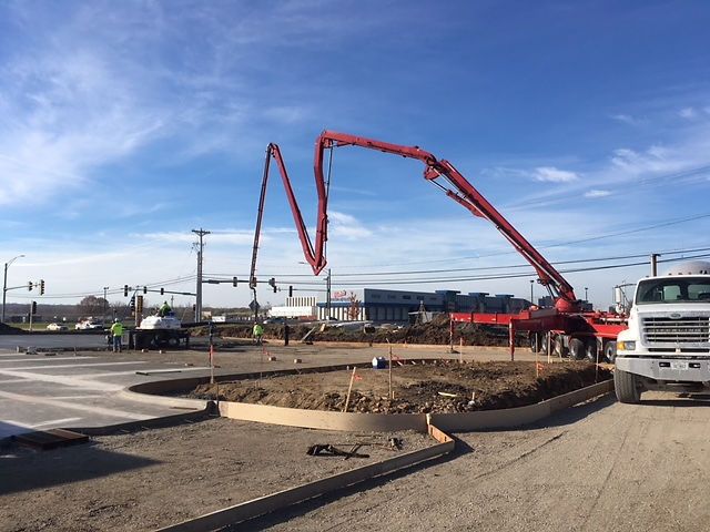 Concrete pump truck pouring concrete at a construction site near a street intersection on a sunny day.
