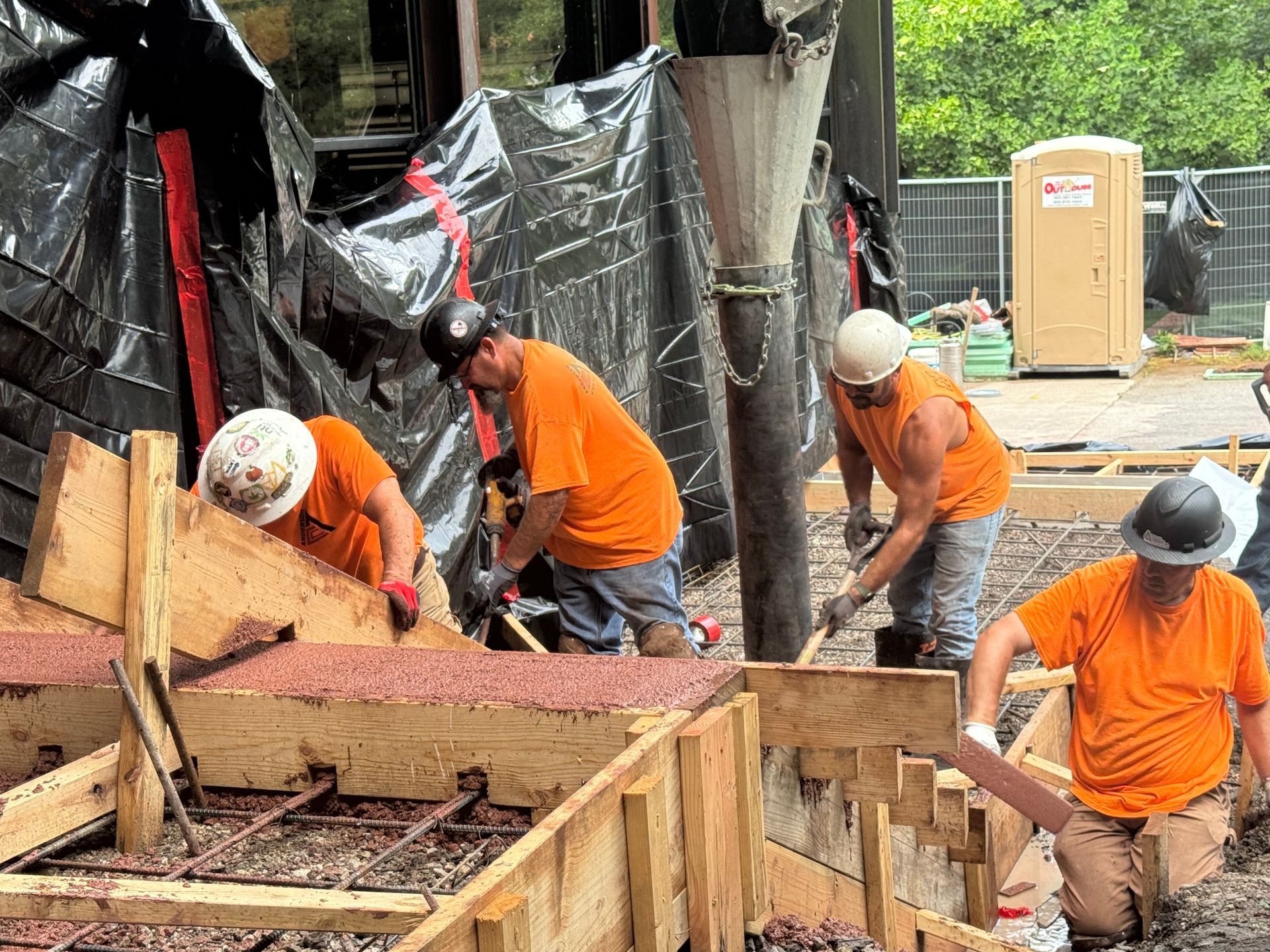 Construction workers pouring and smoothing concrete at a building site, with a cement truck in the background.