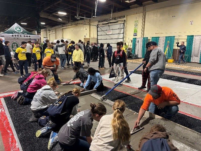 A diverse group of people works together to smooth wet concrete in a large, industrial indoor facility.