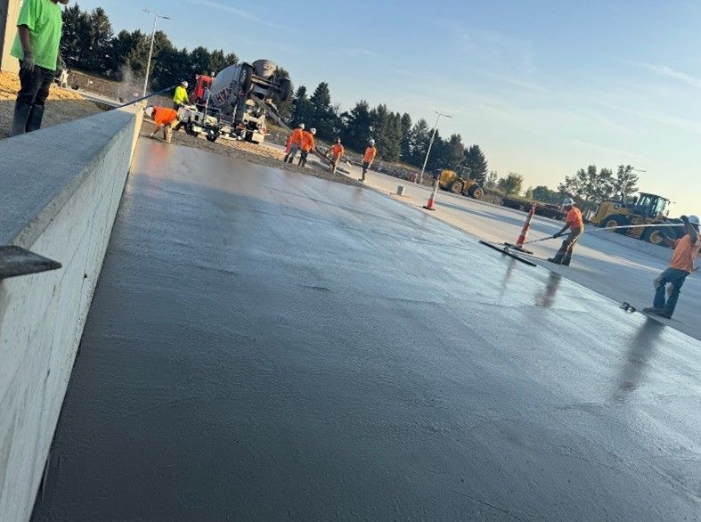 Trucks loading at a warehouse dock, concrete ground, gray building, overcast sky.