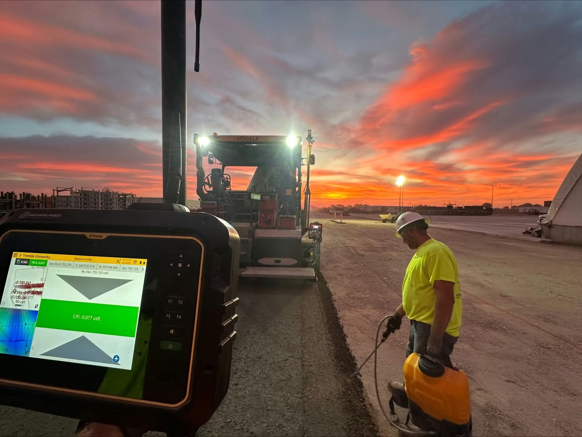 A construction worker with survey equipment on a job site at sunset, with a digital level showing grade status in foreground.