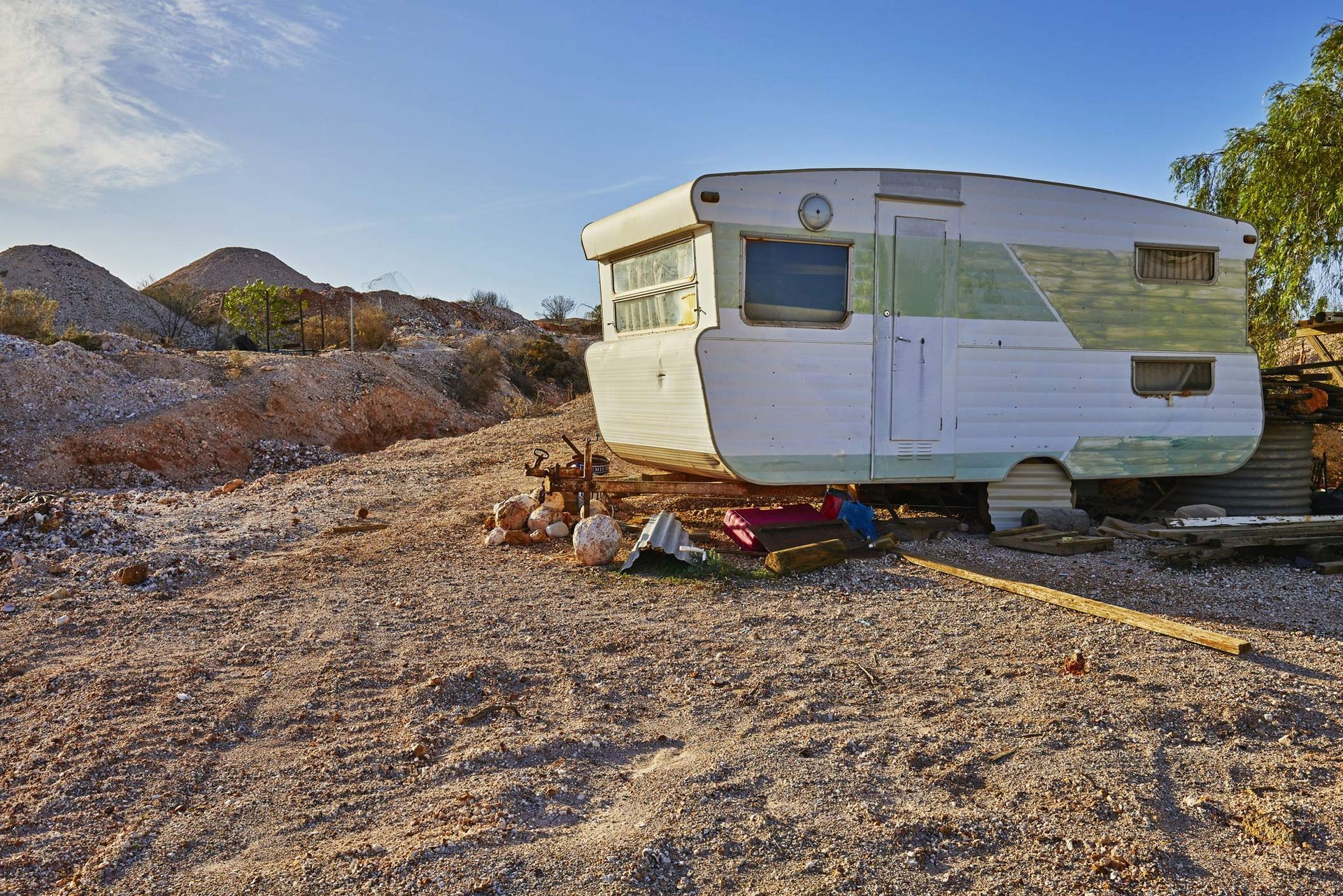 A white caravan is on top of rocky, deserted ground, with small cliffs in the background.