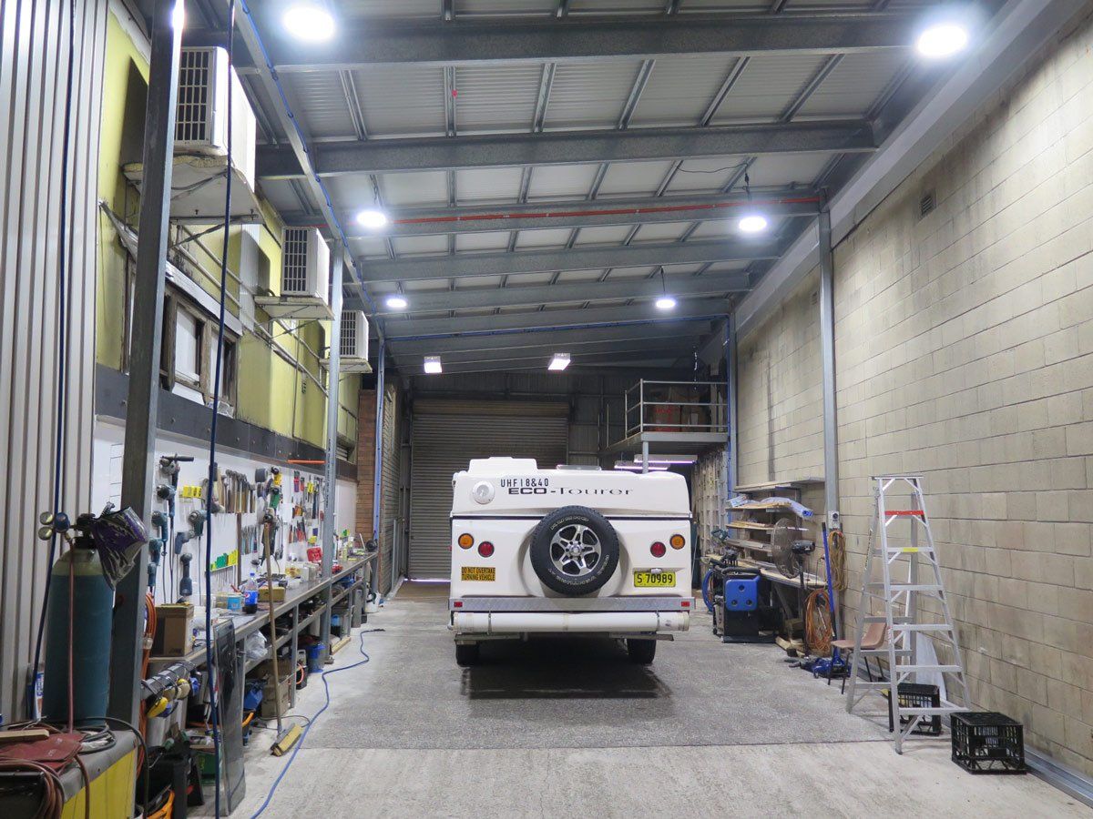 A camper is parked in a garage with lots of tools.