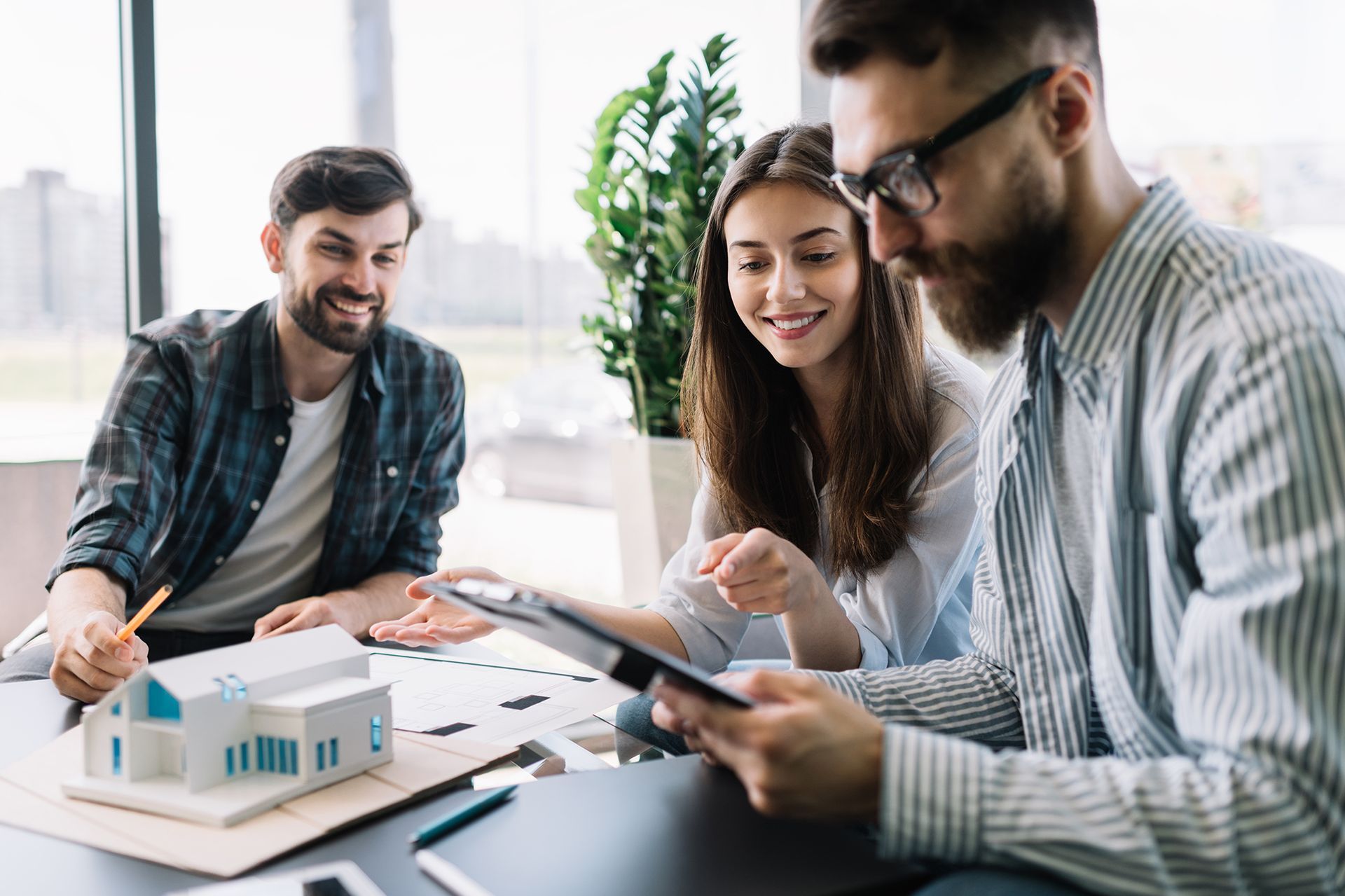 A group of people are sitting at a table looking at a model of a house.