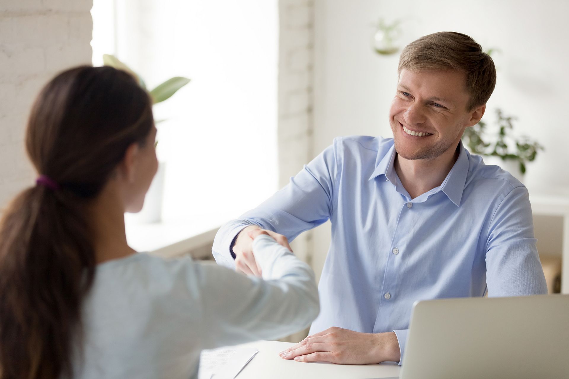 A man and a woman are shaking hands while sitting at a table.