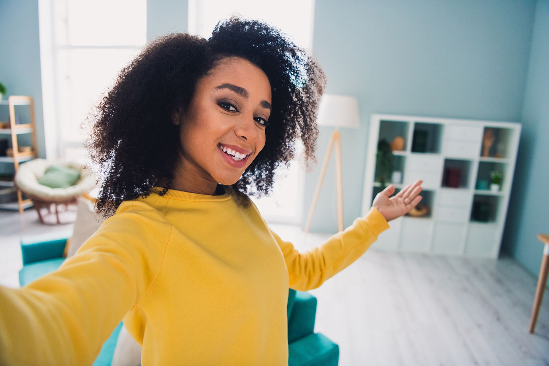 A woman in a yellow sweater is taking a selfie in a living room.