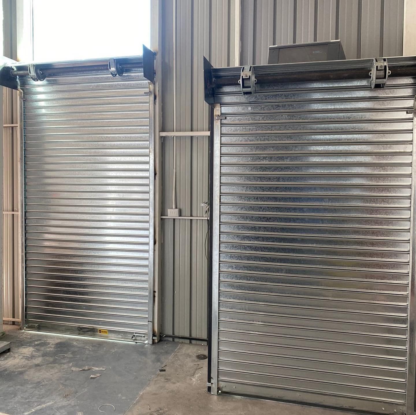 Dos puertas enrollables metálicas cerradas, una al lado de la otra, en un entorno industrial.