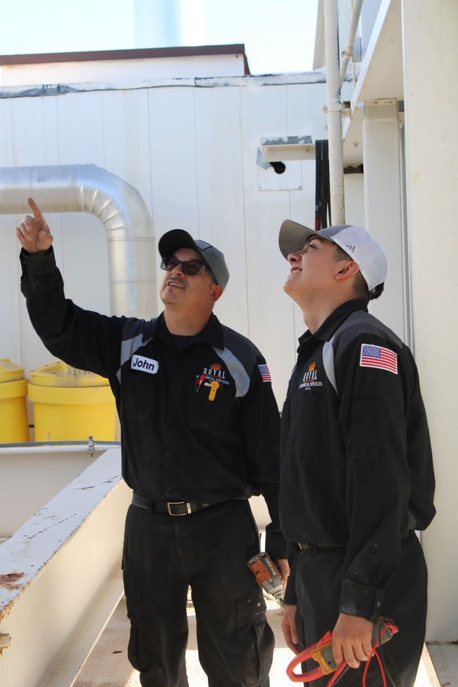 Two men in black uniforms are looking up at something