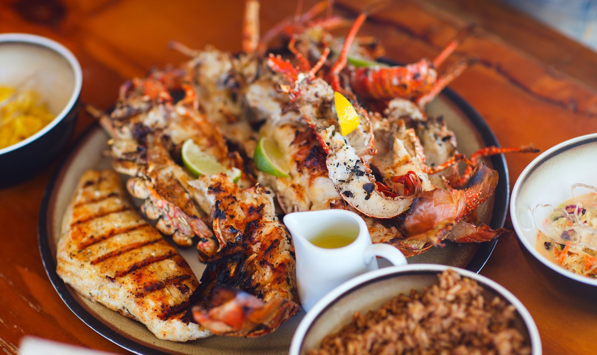 A plate of food with rice , chicken , lobsters and other foods on a wooden table.