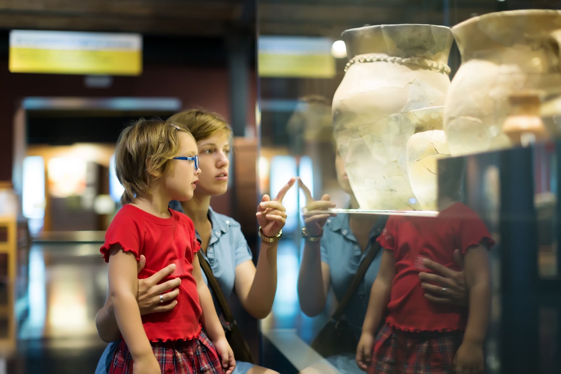 A woman and a little girl are looking at a vase in a museum.