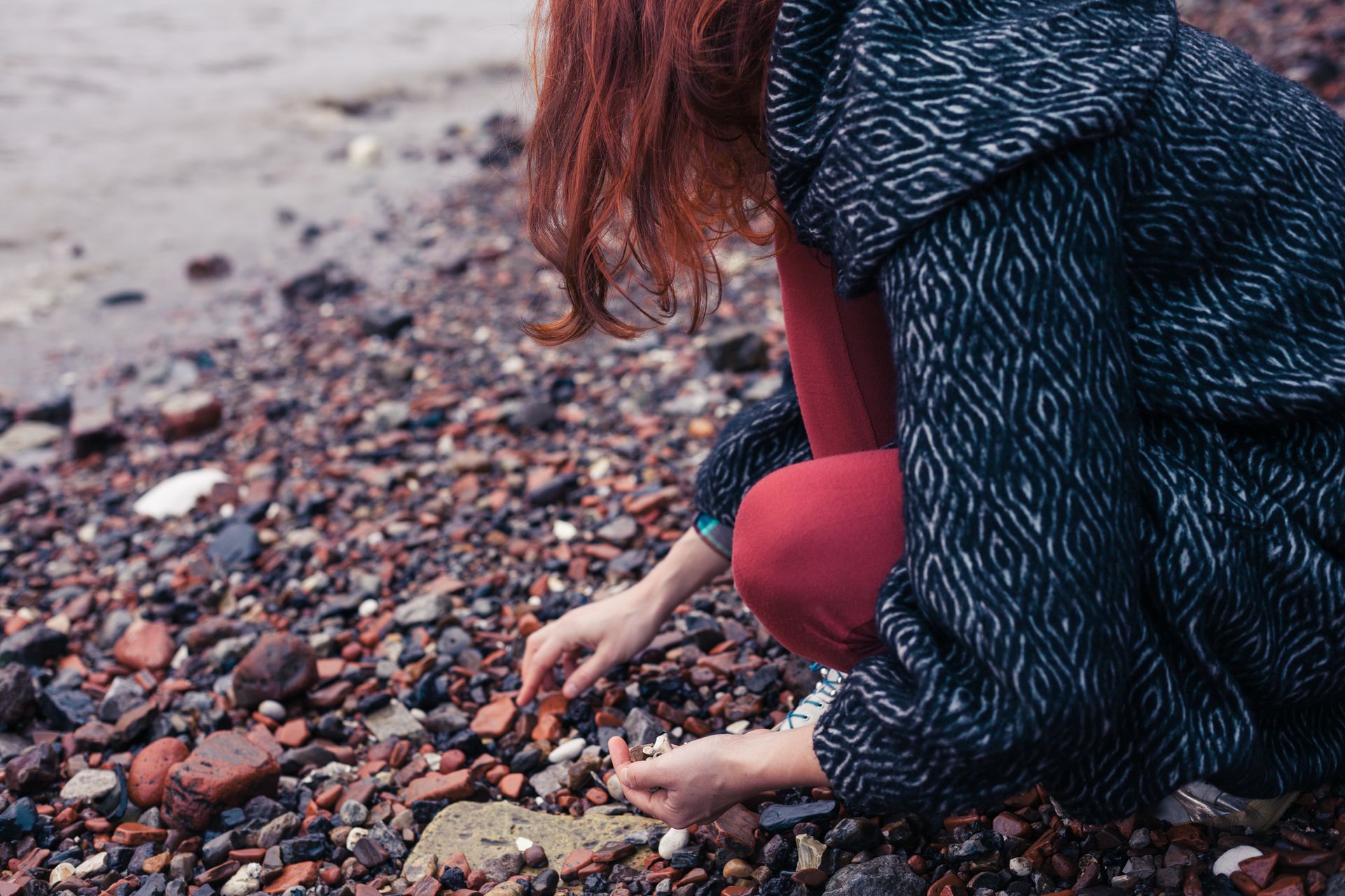 A woman is picking up rocks on the beach.