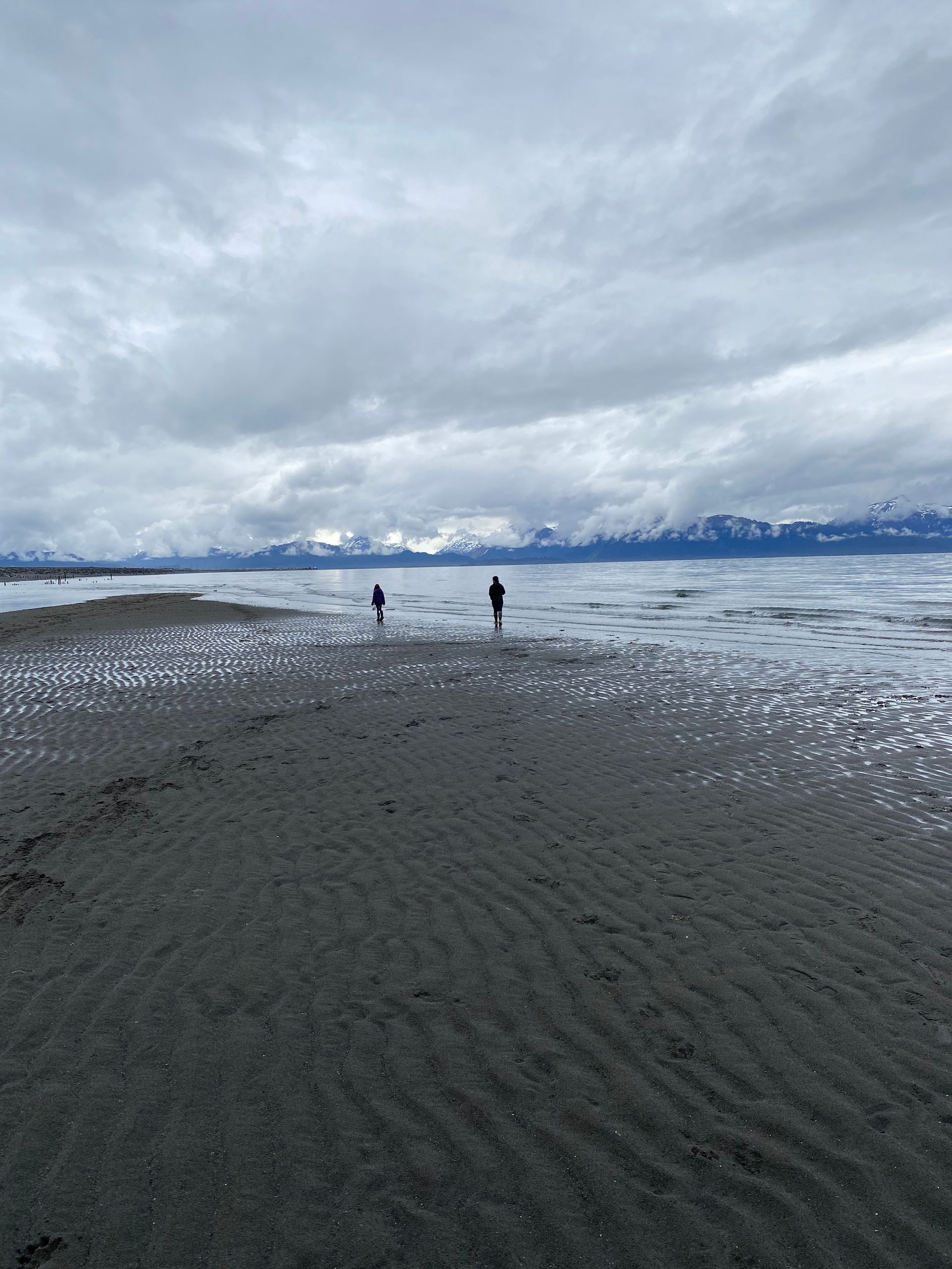 Two people walking on a beach with mountains in the background