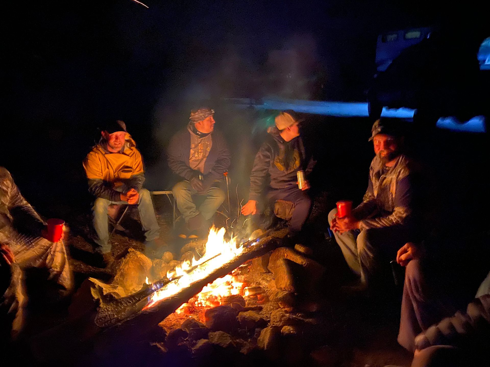 A group of people are sitting around a campfire at night.