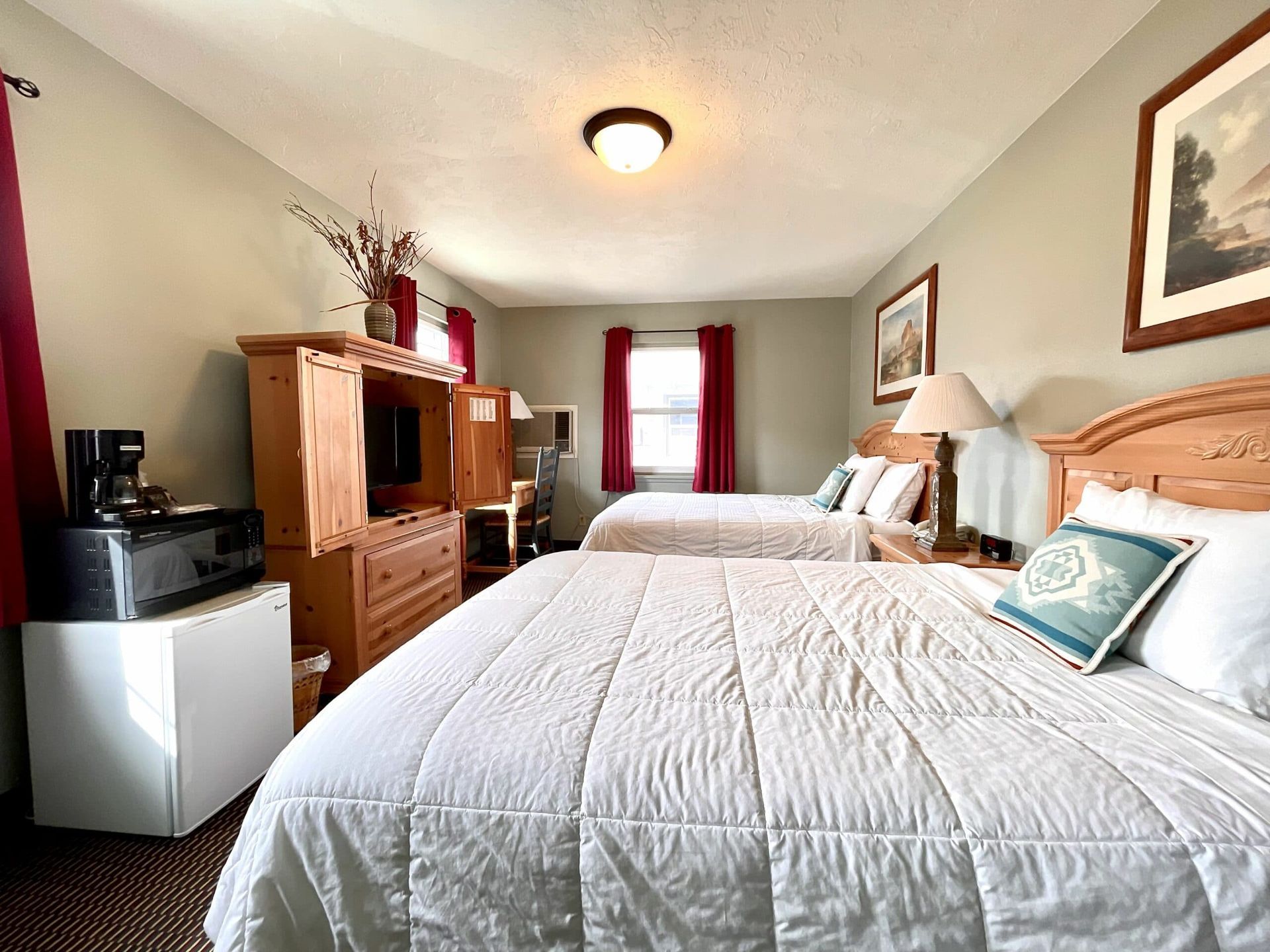A hotel room with two beds , a refrigerator and a television.