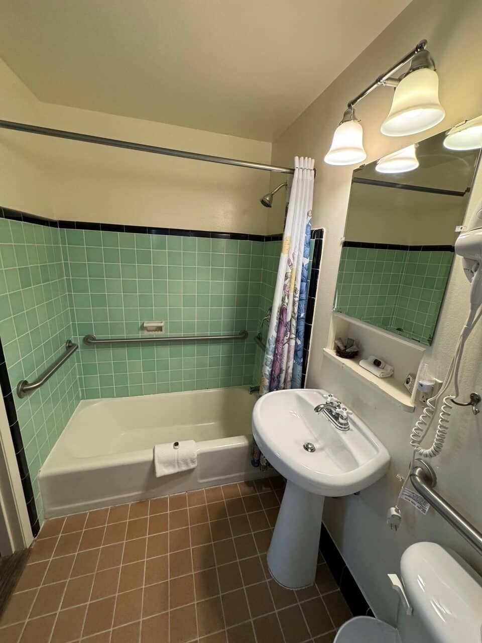 A bathroom with green tiles , a sink , a toilet , and a shower.