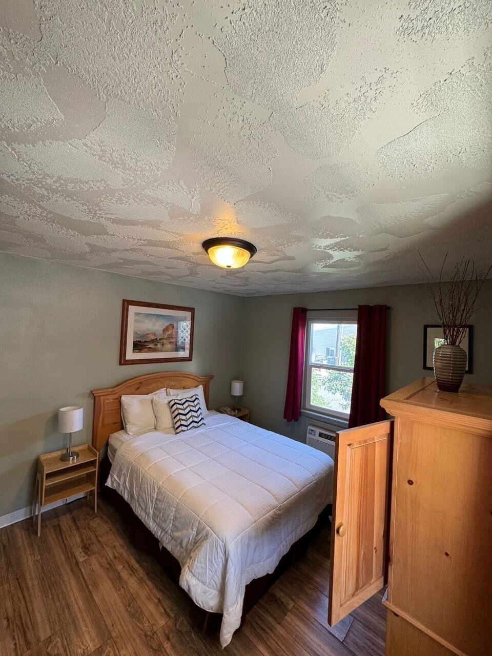 A bedroom with a bed , dresser , nightstand and window.
