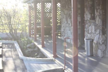 A porch with a sink and a trash can in front of a stone building.