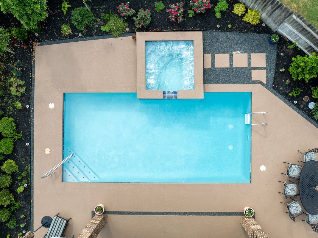 An aerial view of a large swimming pool with a hot tub in the middle.