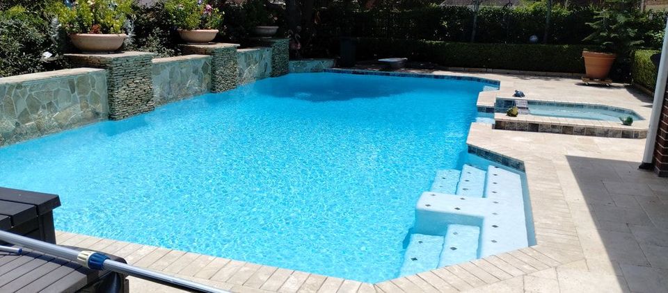 A large swimming pool with stairs and a hot tub in the backyard.