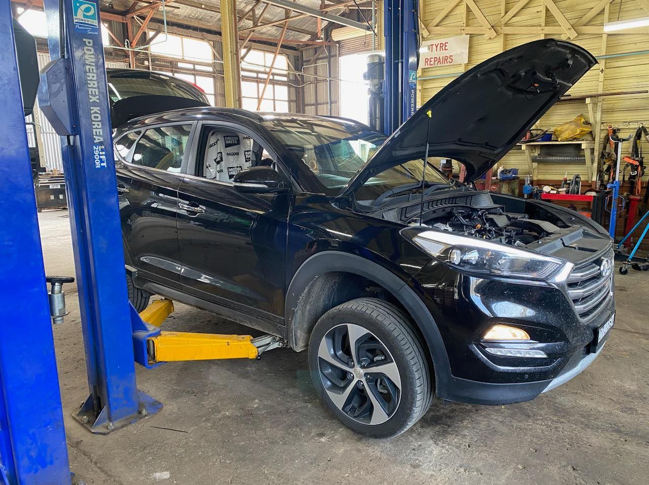 A black car with the hood up is on a lift in a garage. — BDM Heavy Vehicle Repairs In Wauchope, NSW