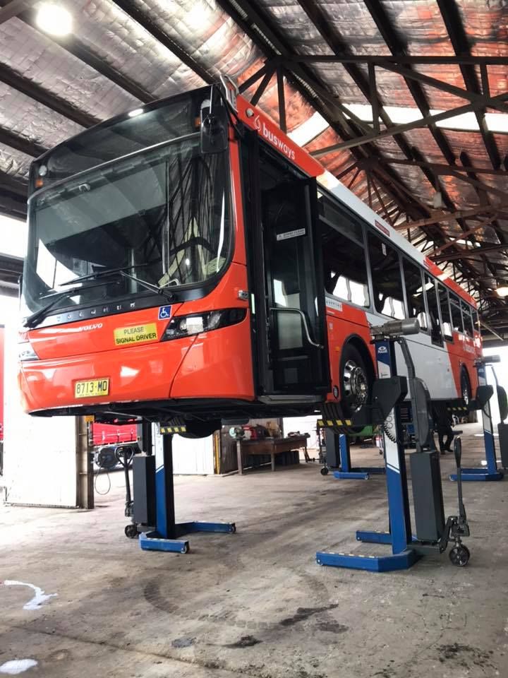 A red bus is sitting on a lift in a garage.— BDM Heavy Vehicle Repairs In Kempsey, NSW