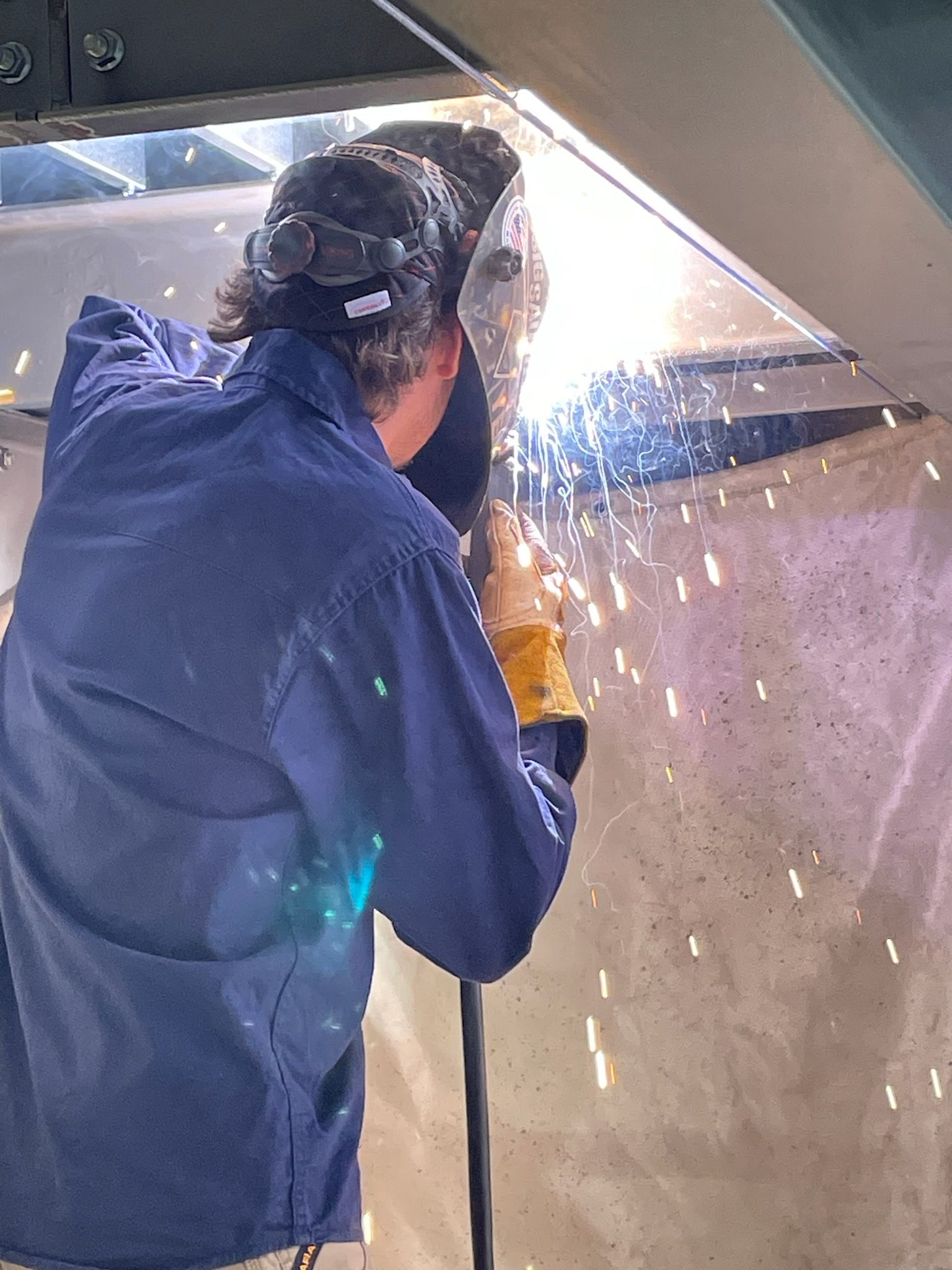 A man wearing a welding mask is welding a piece of metal