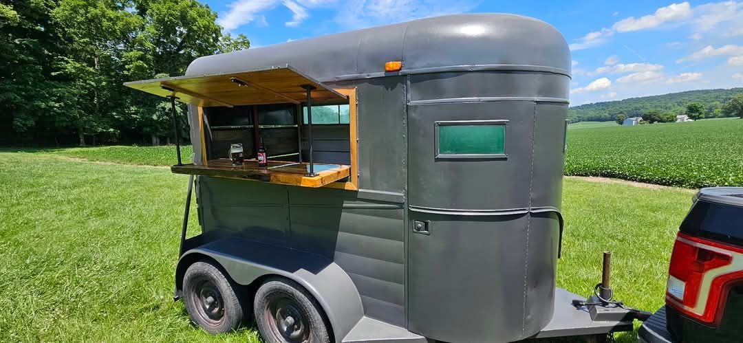 A horse trailer is parked in a grassy field next to a truck.