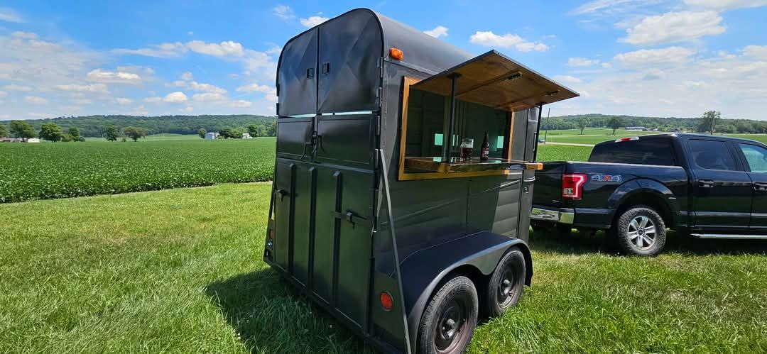A horse trailer is parked in a grassy field next to a truck.